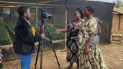 Two women are speaking in front of a camera while a third woman is sitting behind the camera and films them.