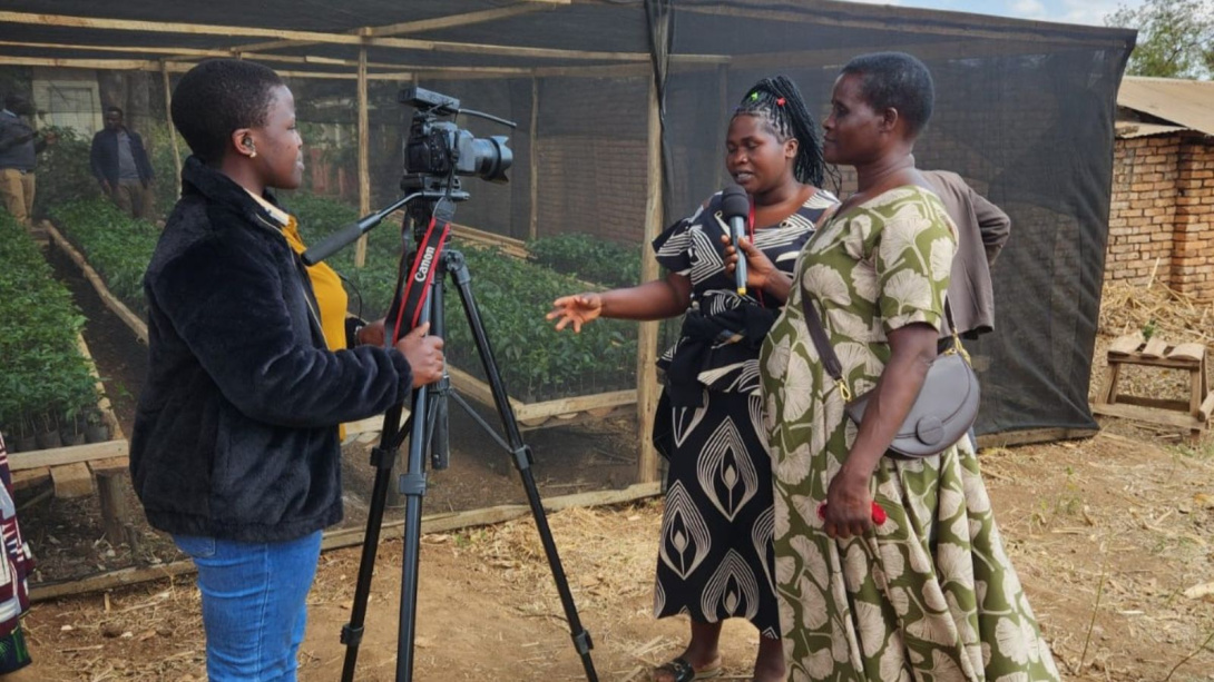 Two women being interviewed while a third is using a DSLR camera to film them.